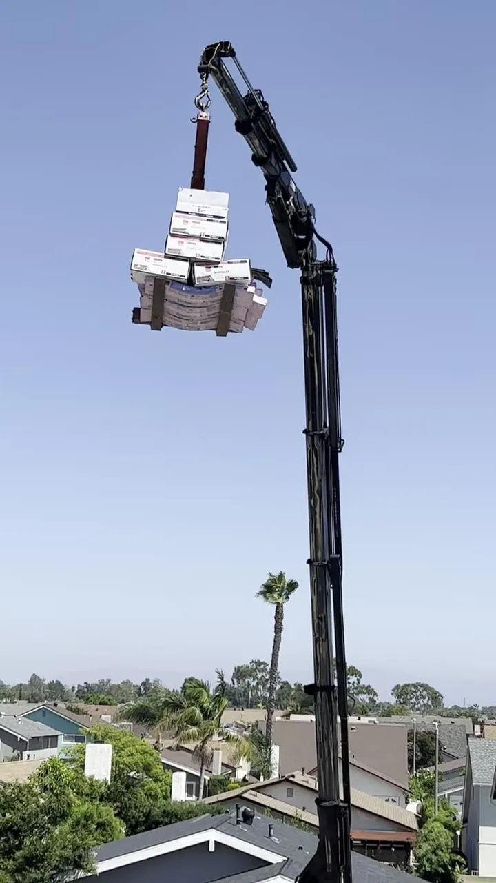 Crane lifting a pallet of shingles to the roof on a Pacific Roofing job